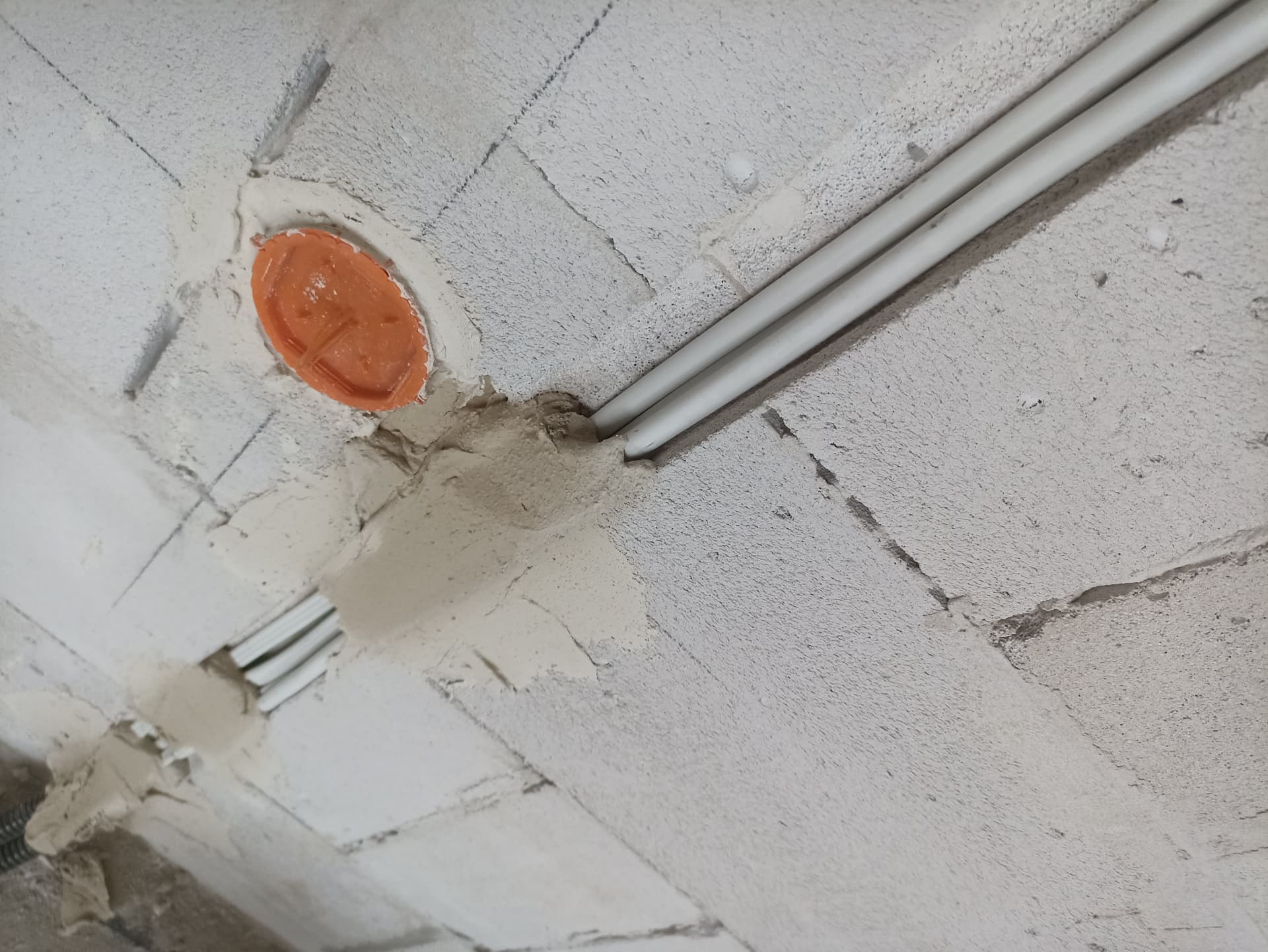 Przewody wprowadzone do pomarańczowej puszki instalacyjnej w ścianie
